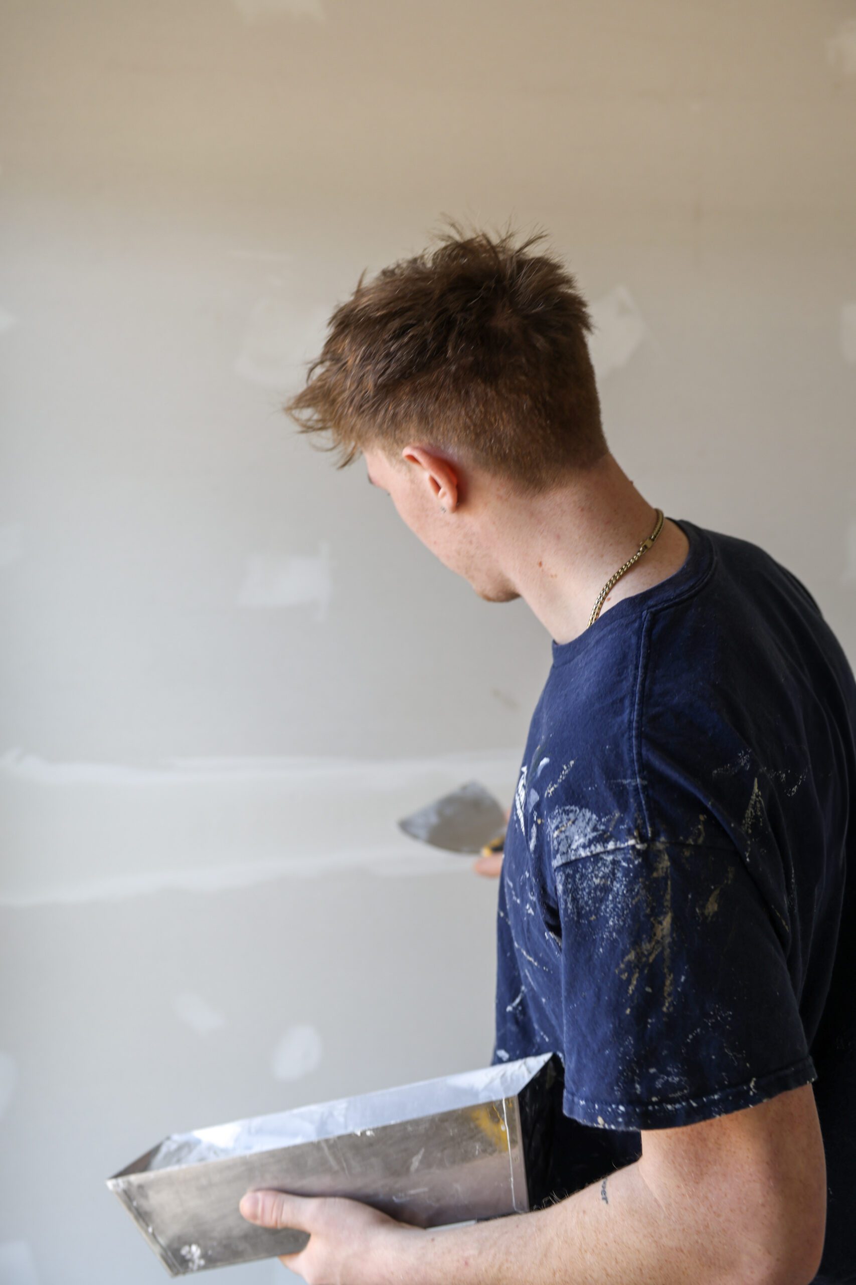 Worker holding pan of drywall mud while applying it to wall during painting and drywall services by expert team for residential and commercial projects