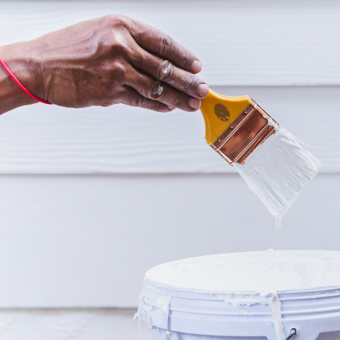 Hand dipping paint brush into paint bucket showing painting and drywall services tools used by expert team for residential and commercial projects