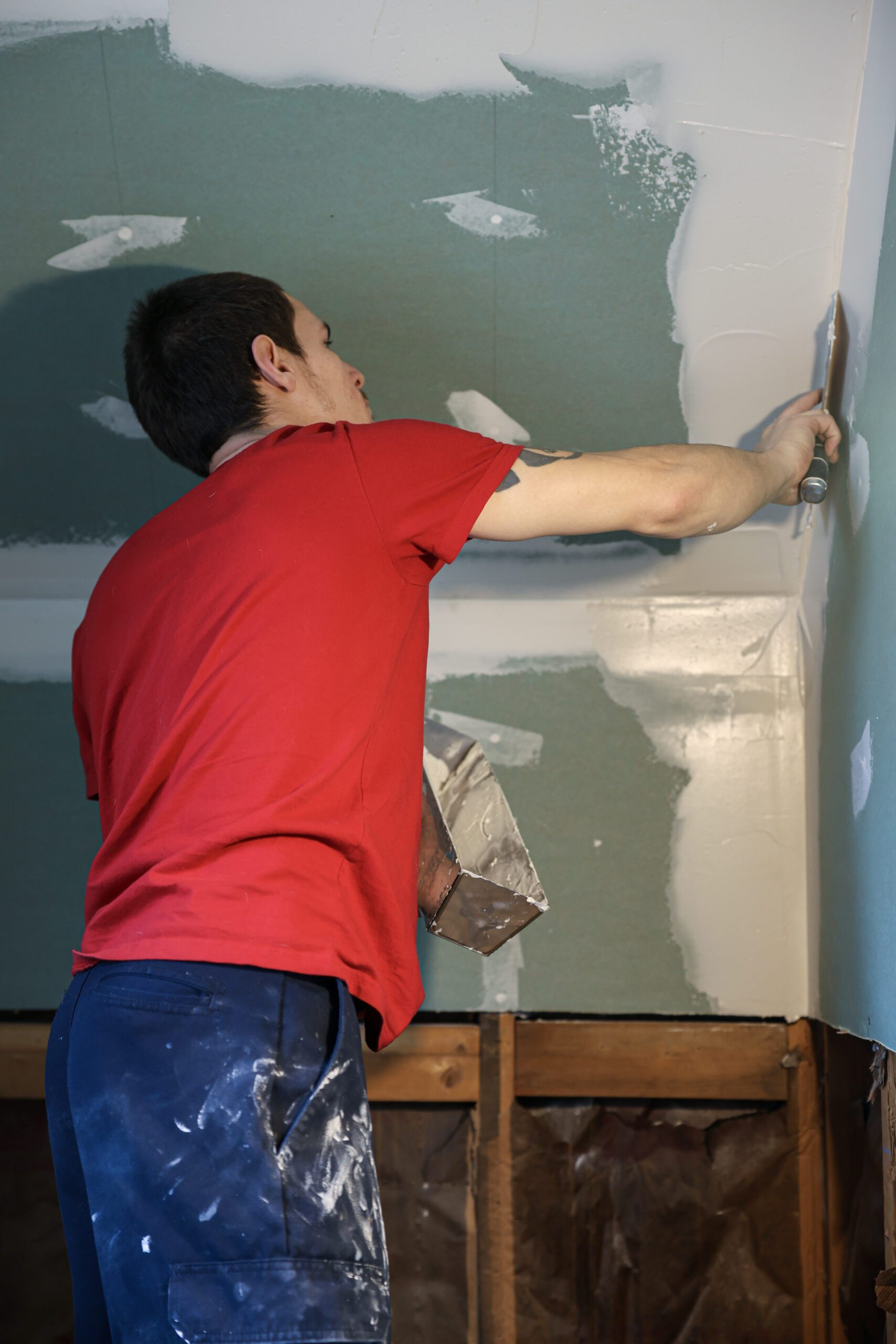 Man on ladder applying drywall mud to ceiling during painting and drywall services installation by expert team for residential and commercial property renovation